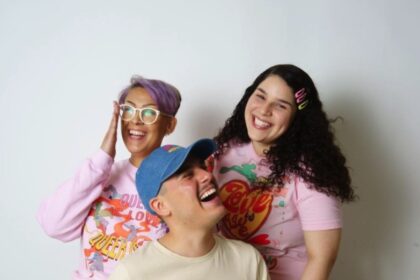3 LGBTQIA+ people stand wearing various designs from gay pride apparel
