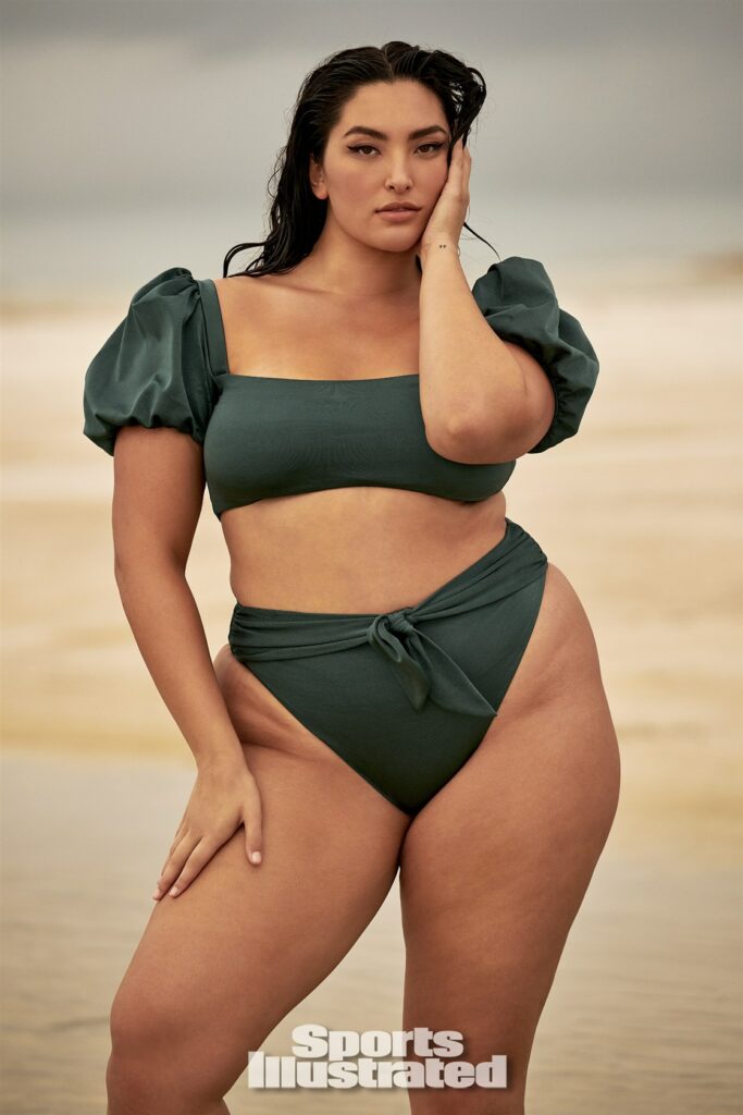 Asian curve model Yumi Nu poses for the camera, with her hand on her face, with an olive green two-piece bathing suit.