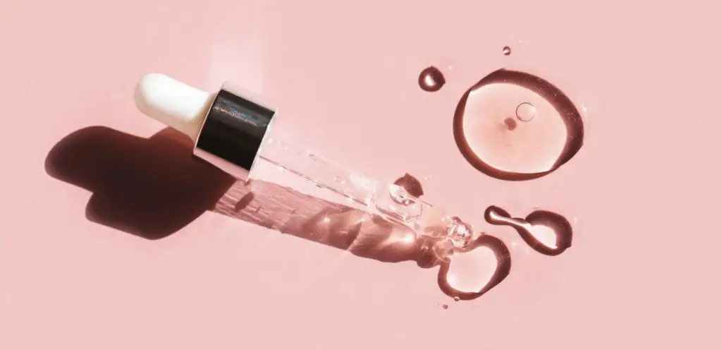 small-dropper-with-clear-liquid-against-pink-background.-skincare-