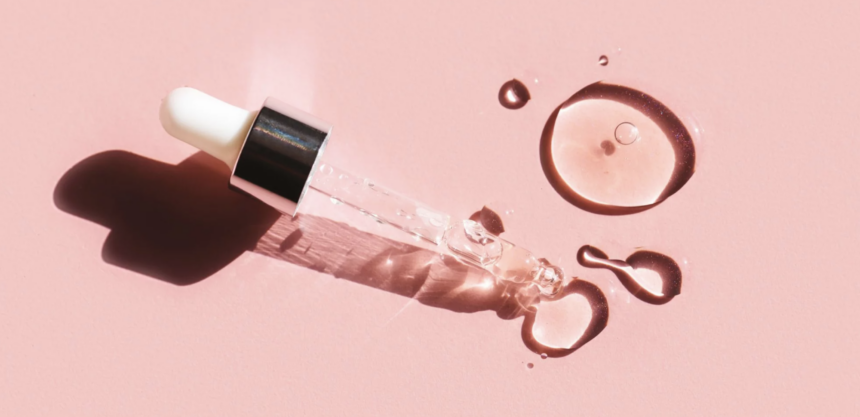 small dropper with clear liquid against pink background. skincare