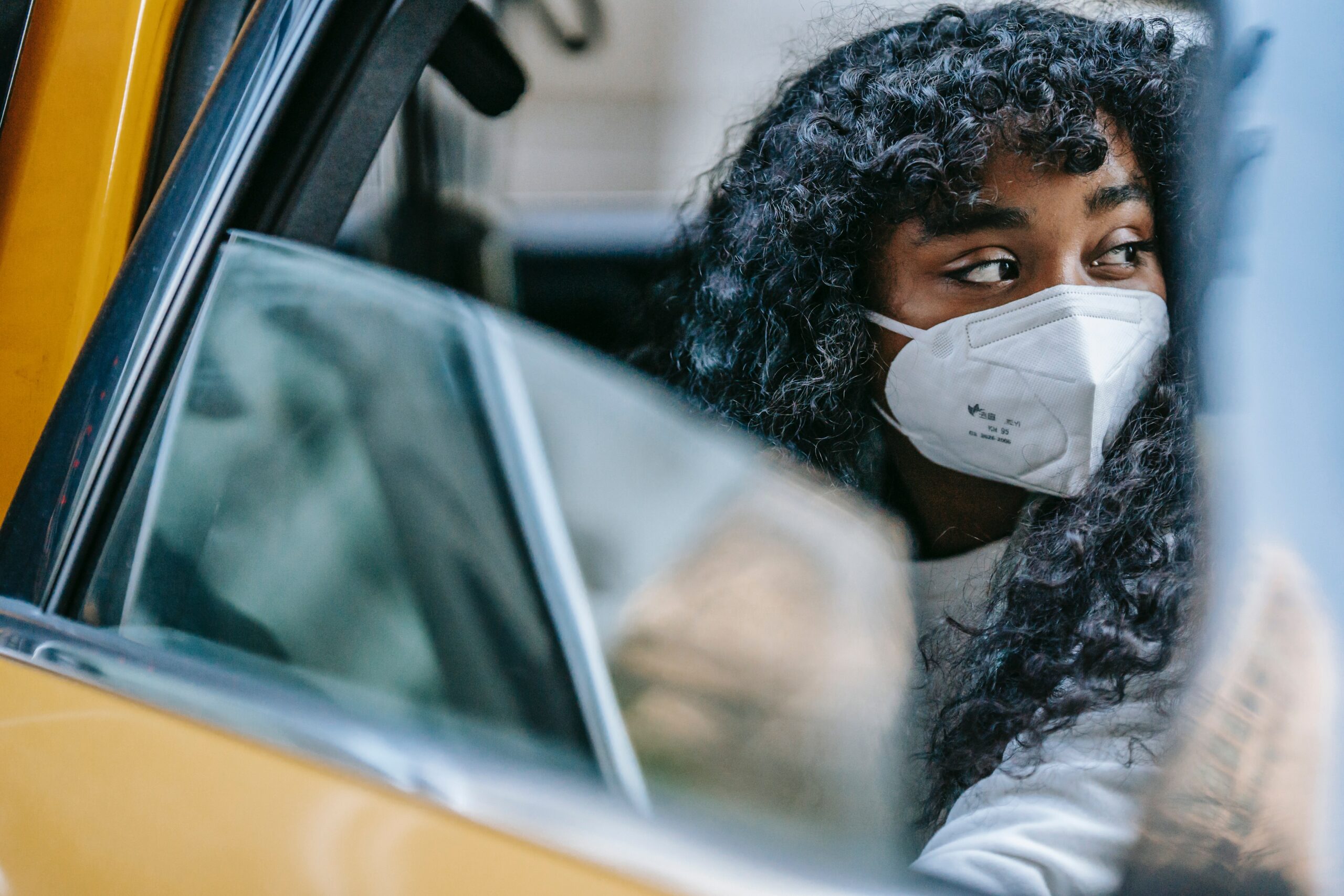 A Black person sits in a taxi wearing an N95 mask. Post Pandemic Plus Size Travel