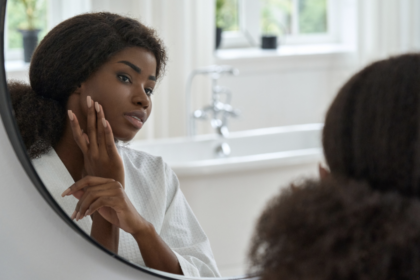 Attractive Black Young Woman Touching Face Skin Looking in Mirror.