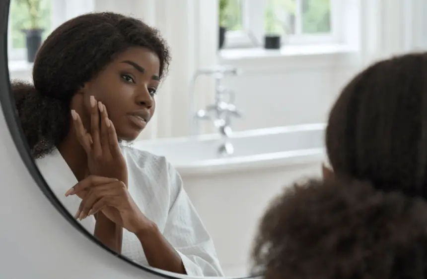 Attractive Black Young Woman Touching Face Skin Looking in Mirror.
