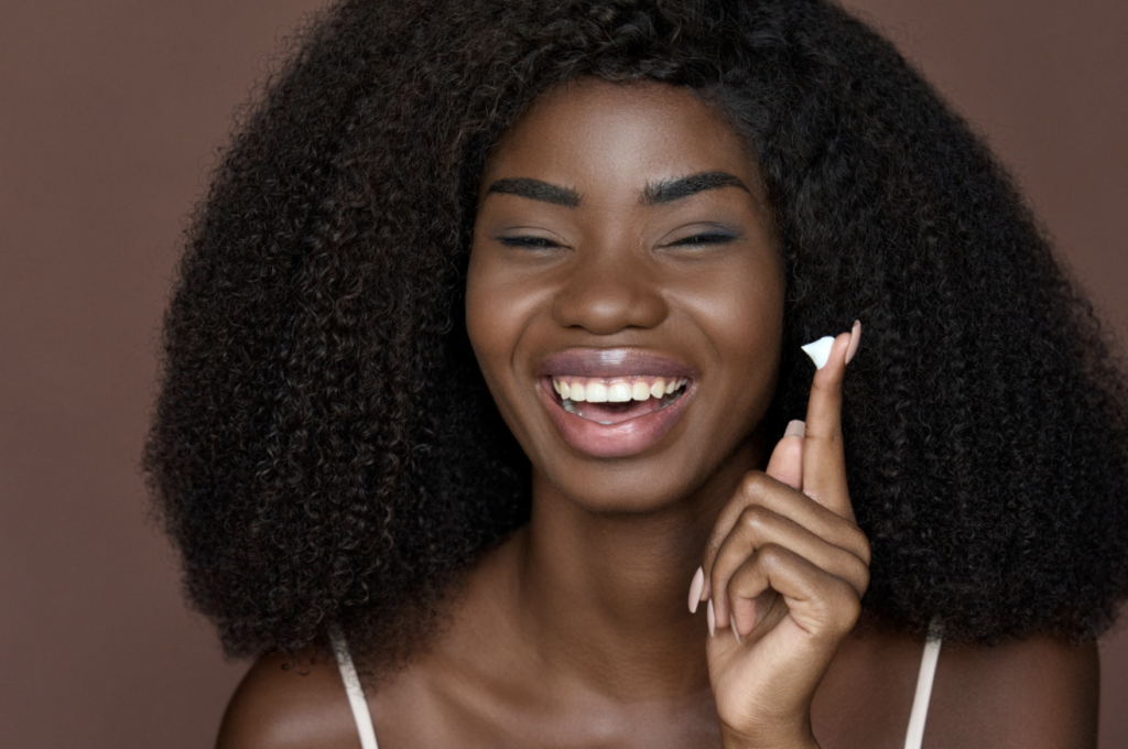 Happy Young Black Woman Applying Facial Cream