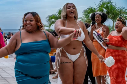 Nina Sharae in a blue dress and a model in a white plus size swimwear smiling during The Nina Sharae Experience runway show during Miami Swim Week