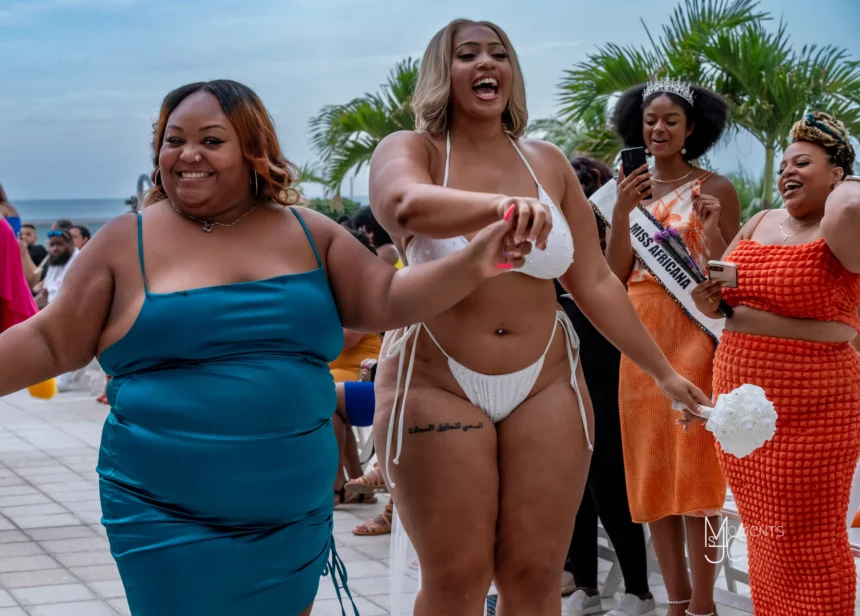 Nina Sharae in a blue dress and a model in a white plus size swimwear smiling during The Nina Sharae Experience runway show during Miami Swim Week