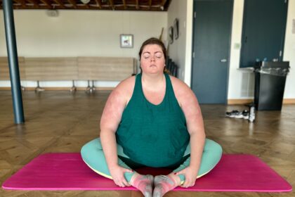 white plus size woman with hair braided back, matching teal yoga set, sitting on a yoga mat in meditation