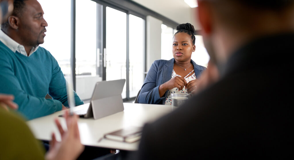 Unposed shot of black professional female talking with team of diverse mixed race businesspeople in large modern office working on collaboration and teamwork strategies