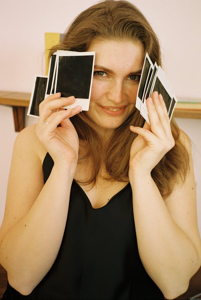A happy woman holding polaroid photos while smiling indoors.