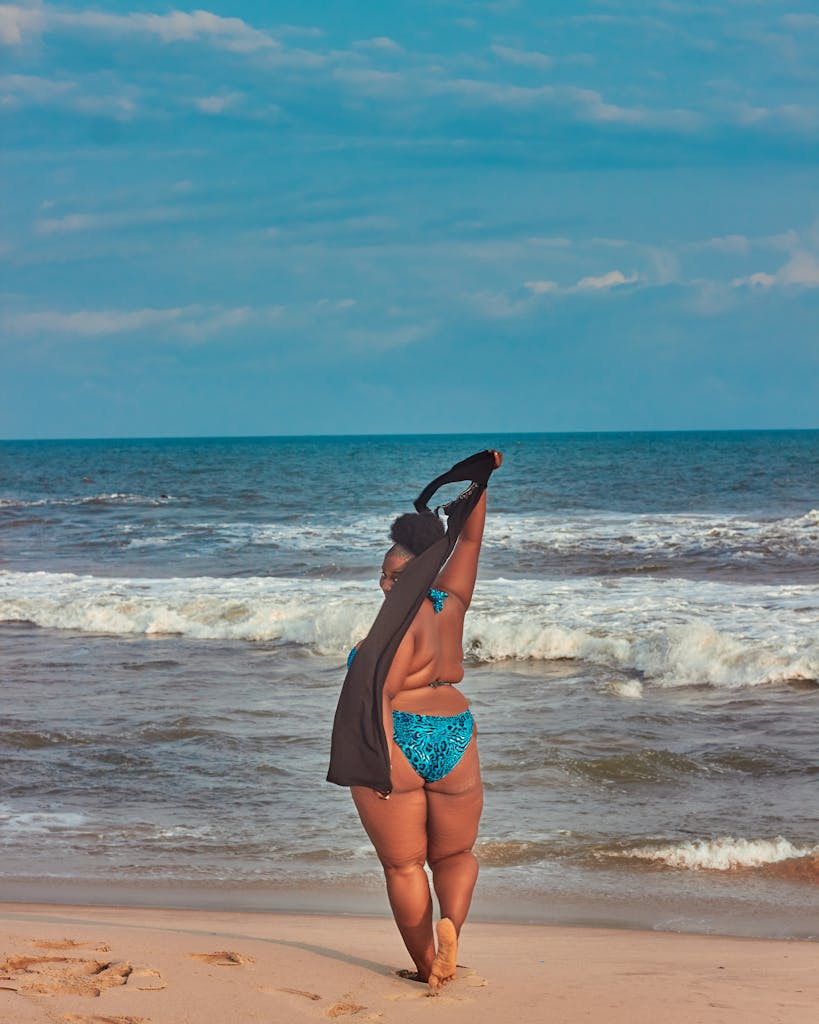 A woman enjoying summer at the beach in a blue bikini, embracing the ocean breeze. 5 Plus Size Travel Packing Tips That Make Every Trip Easier