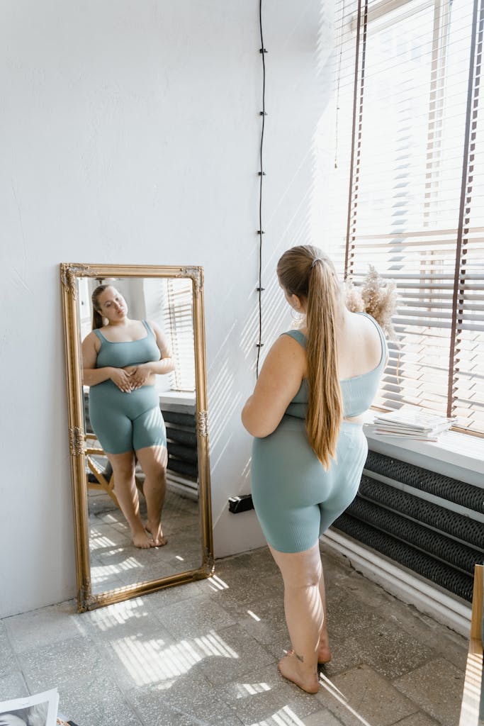 Confident plus size woman in activewear looking at her reflection, embracing body positivity.