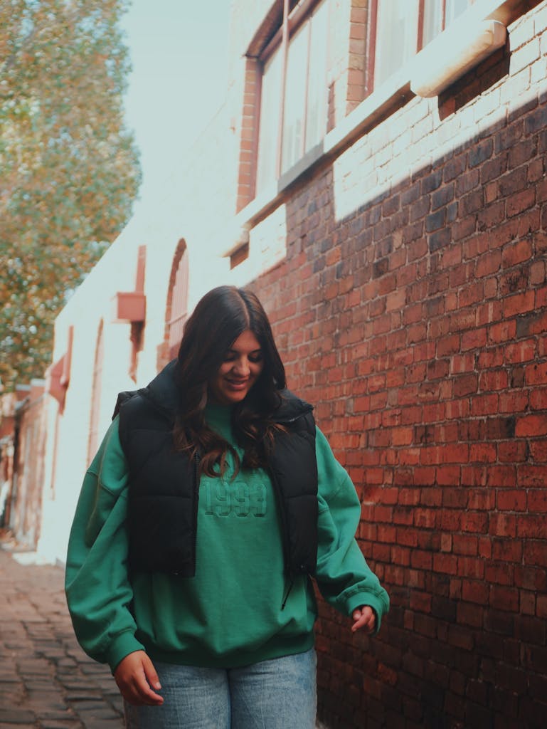 Fashionable woman in a green jacket walks down a brick alley in Melbourne, Australia. Plus size travel confidence.