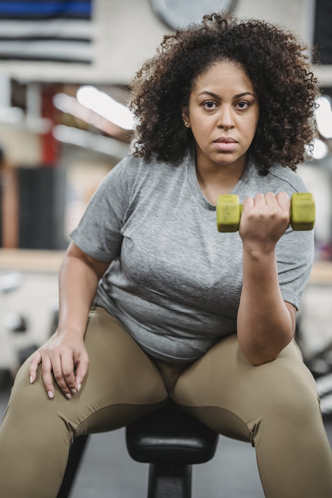 Focused woman exercising with a dumbbell, promoting fitness and strength in a gym setting.
