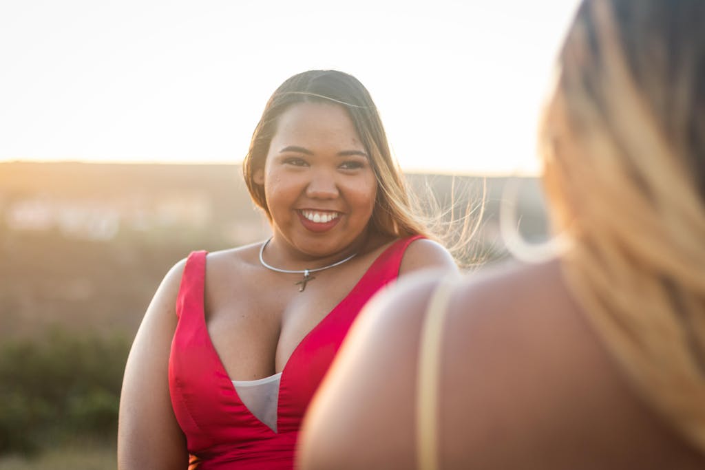 Happy woman in a red dress smiling outdoors at sunset, with blurred background.