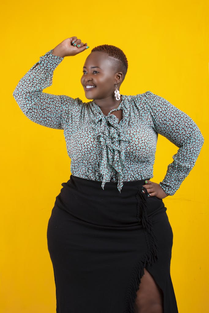 Plus-size black woman with bright smile, green blouse, against vibrant yellow background. Body positivity and confidence.