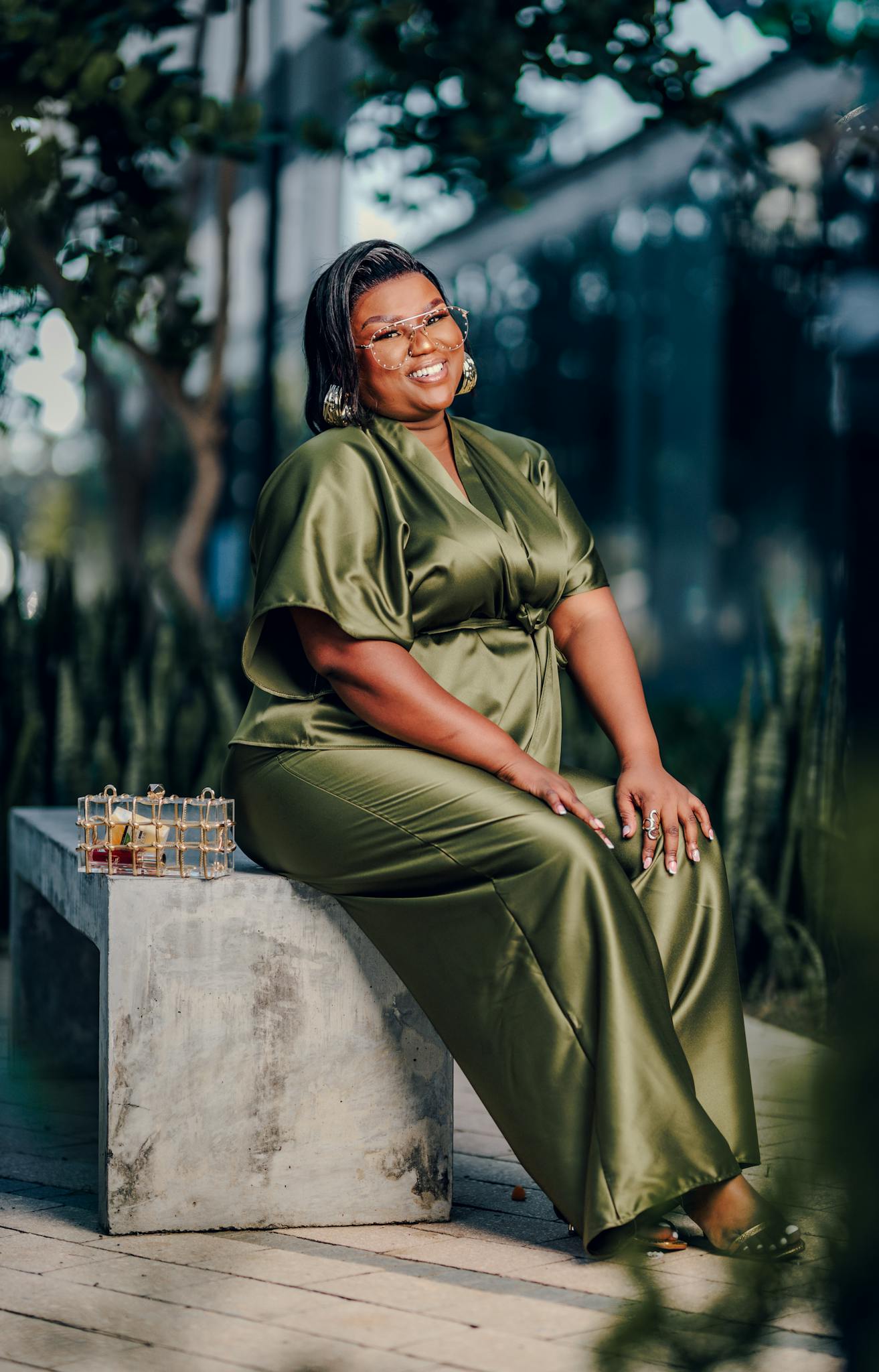 Smiling woman in a green gown sits outdoors on a bench with a small gift box beside her.
posture tips for plus size women