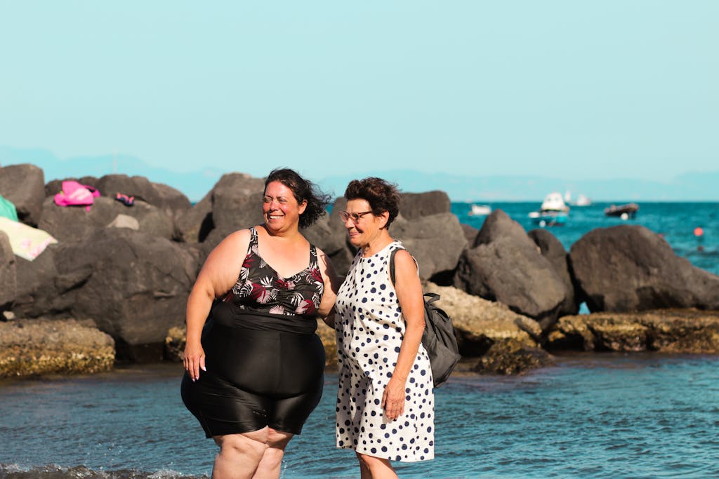 Two women standing by the rocks at a sunny beach in Ischia, Campania, Italy.
