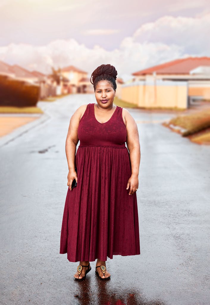 Young African American woman standing confidently in a red dress on a suburban street.
