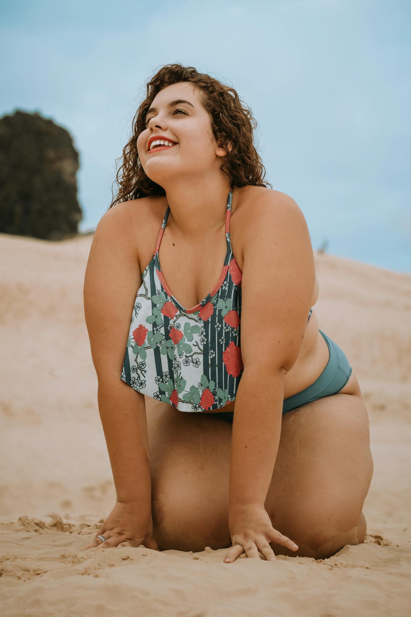 A cheerful woman poses confidently on a sandy beach under a clear blue sky, showcasing summer vibes and body positivity.
plus size confidence in 2026