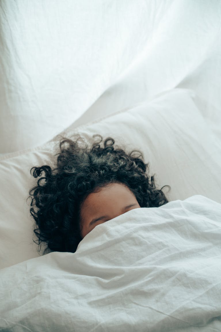 A person with curly hair sleeping peacefully under a white blanket, creating a sense of calm. plus size burnout signs