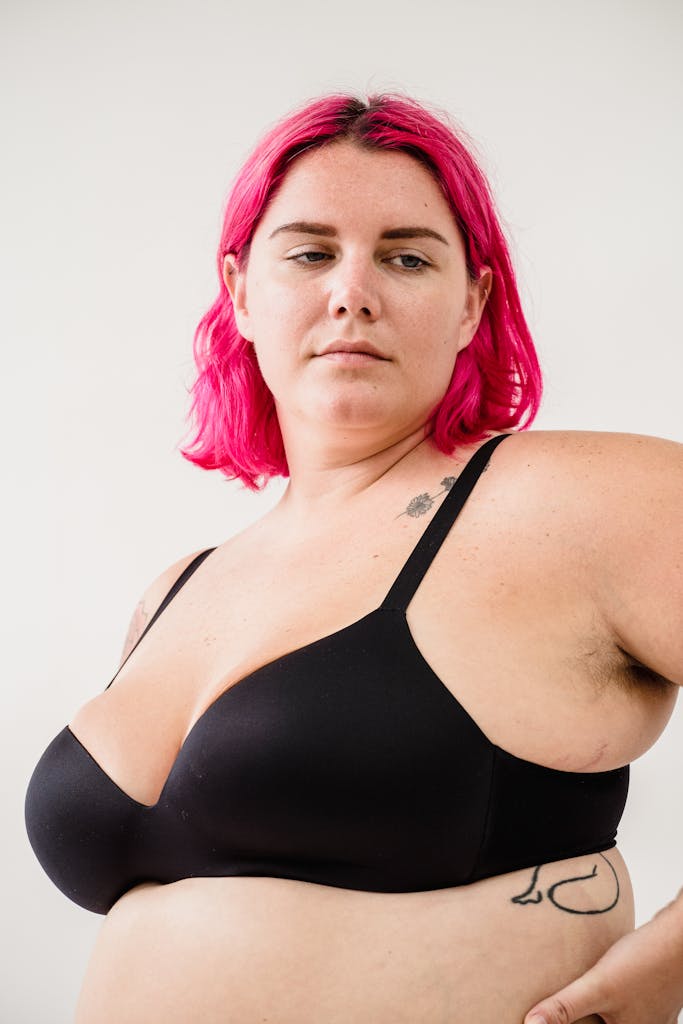 Confident portrait of a woman with pink hair, tattoo, and black bra.