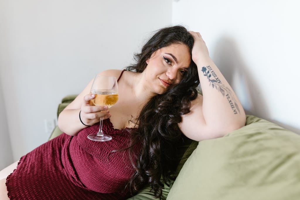 Curvy woman in maroon dress relaxing on a green sofa, enjoying a glass of wine.

radical self care for plus size people