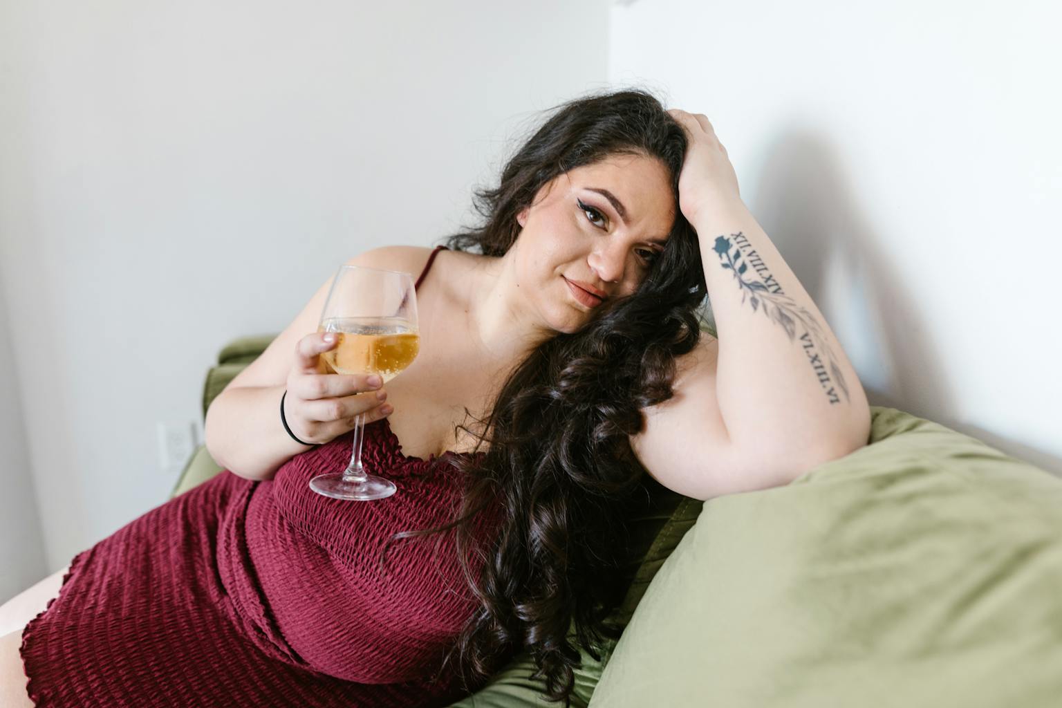 Curvy woman in maroon dress relaxing on a green sofa, enjoying a glass of wine.
radical self care for plus size people