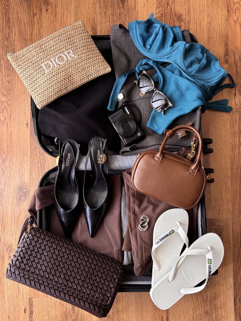 Flat lay of fashion and travel essentials in an open suitcase on wooden floor, ready for vacation.