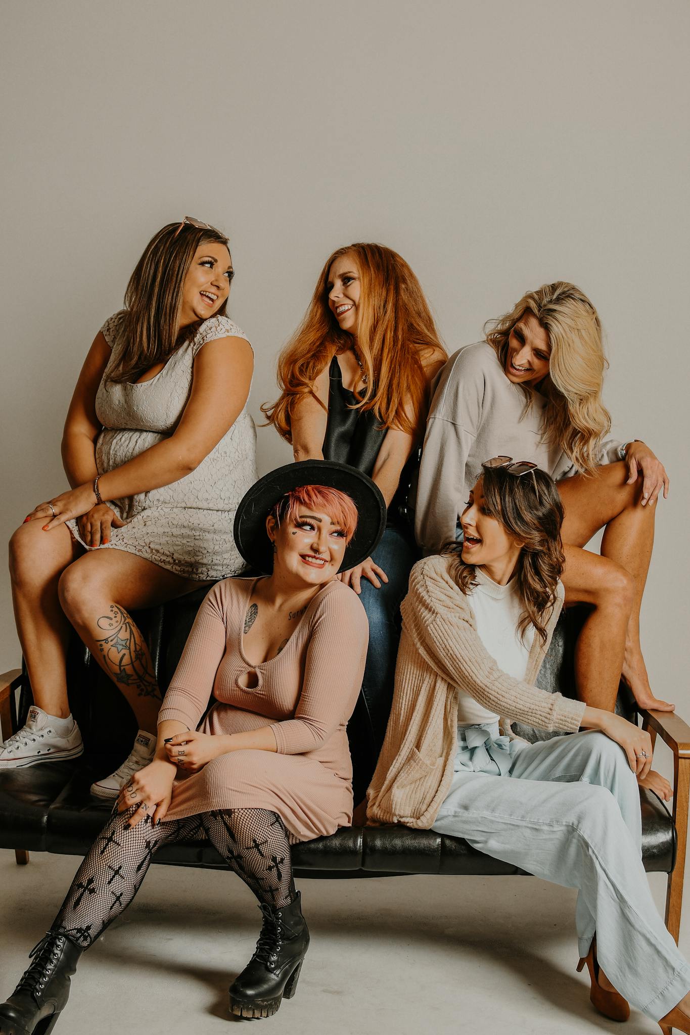 Group of cheerful models with different body types hairstyles and outfits sitting on couch showing authentic friendship types.