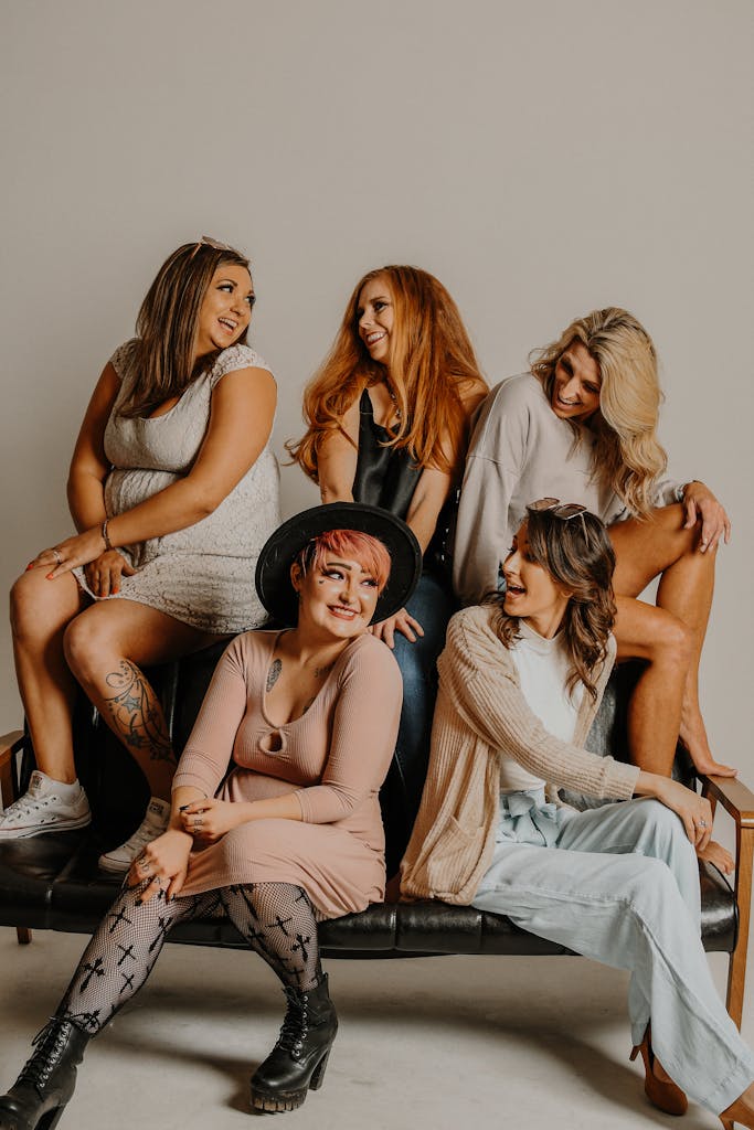 Group of cheerful models with different body types hairstyles and outfits sitting on couch showing authentic friendship types.