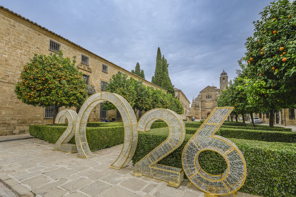 Scenic view of Úbeda, Spain featuring historic architecture and a large 2026 installation amidst orange trees and manicured hedges.

gentle beginnings
