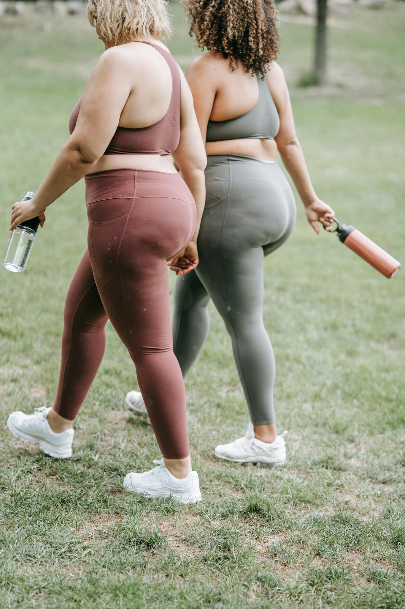 Two women walking on grass in sports clothing, holding water bottles. Focus on fitness and outdoor exercise.
plus size sports bra support