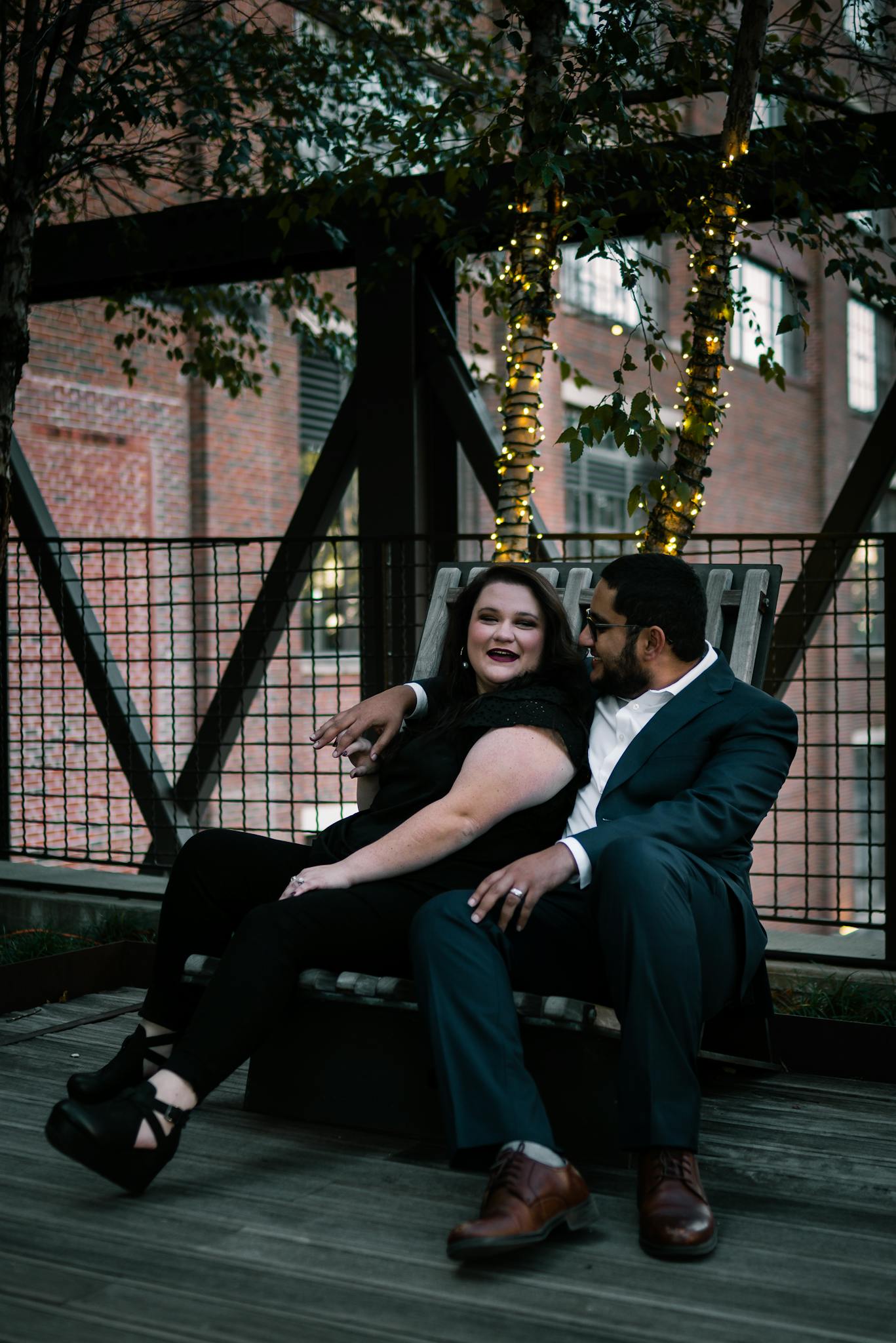 A couple sitting together, embracing on an outdoor terrace with string lights.