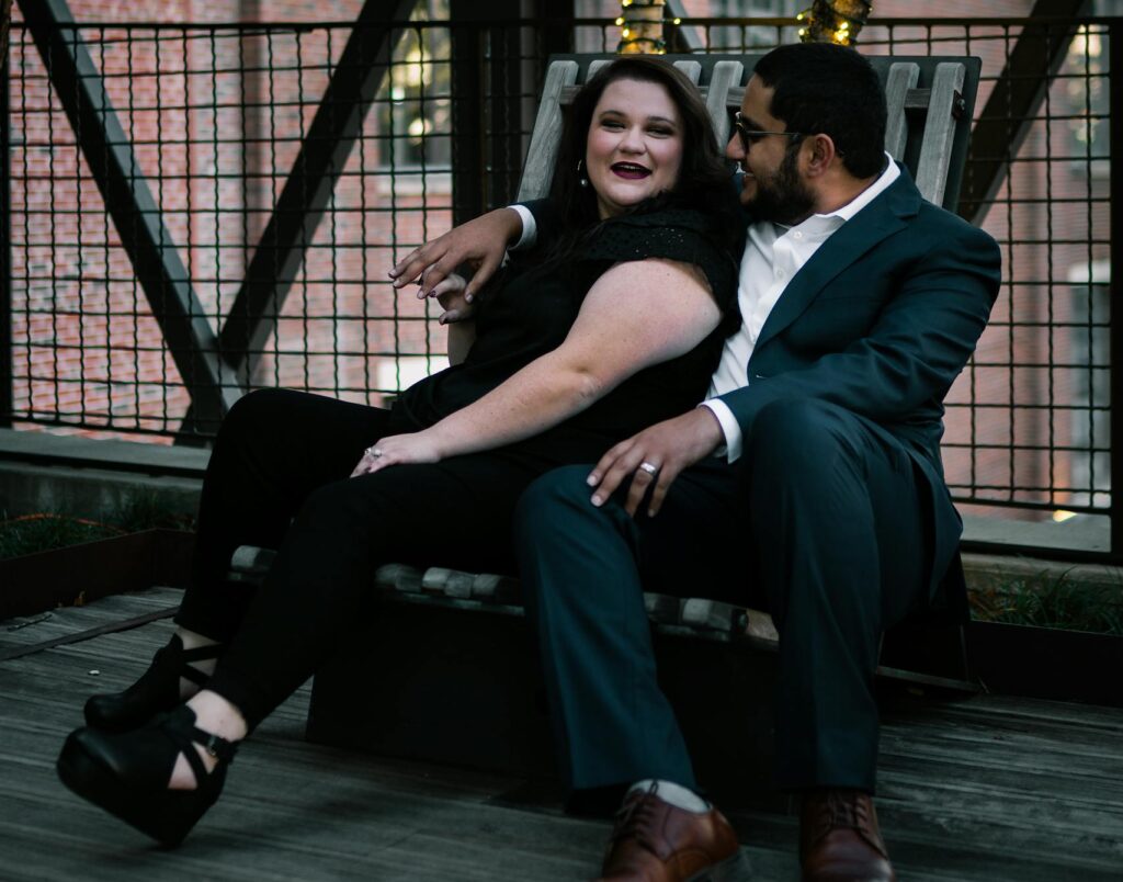 A couple sitting together, embracing on an outdoor terrace with string lights.