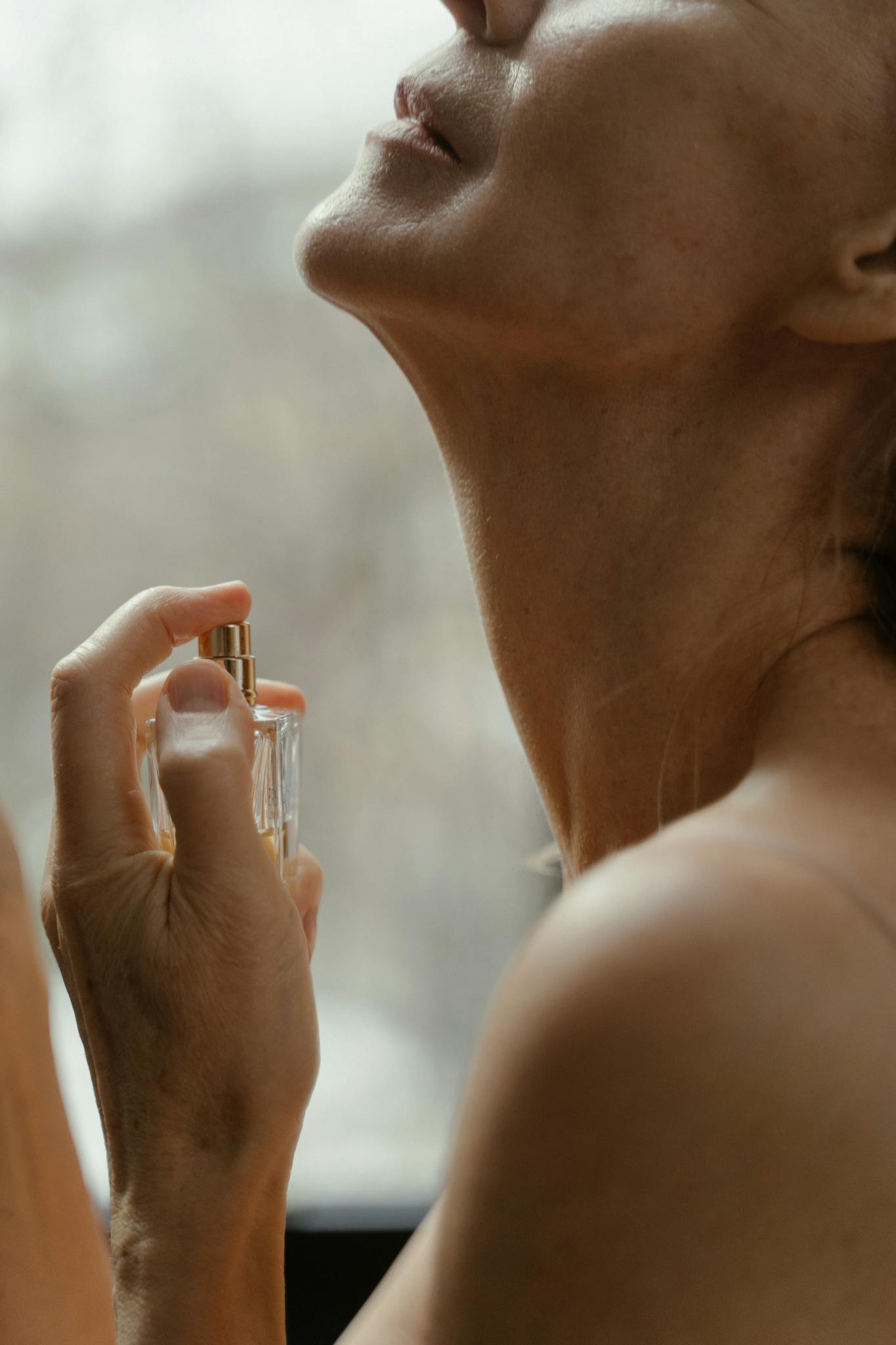 Close-up of a woman gracefully applying perfume to her neck, creating an intimate and sophisticated ambiance.