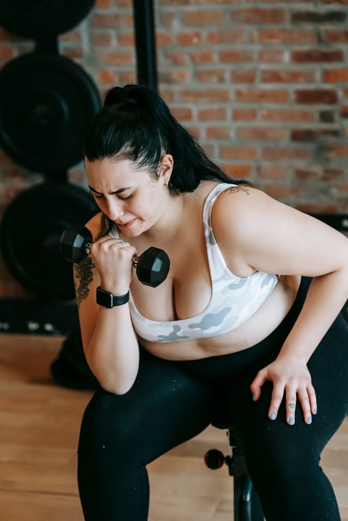 Plus-size woman intensely lifting dumbbell in a gym, showcasing strength and dedication.