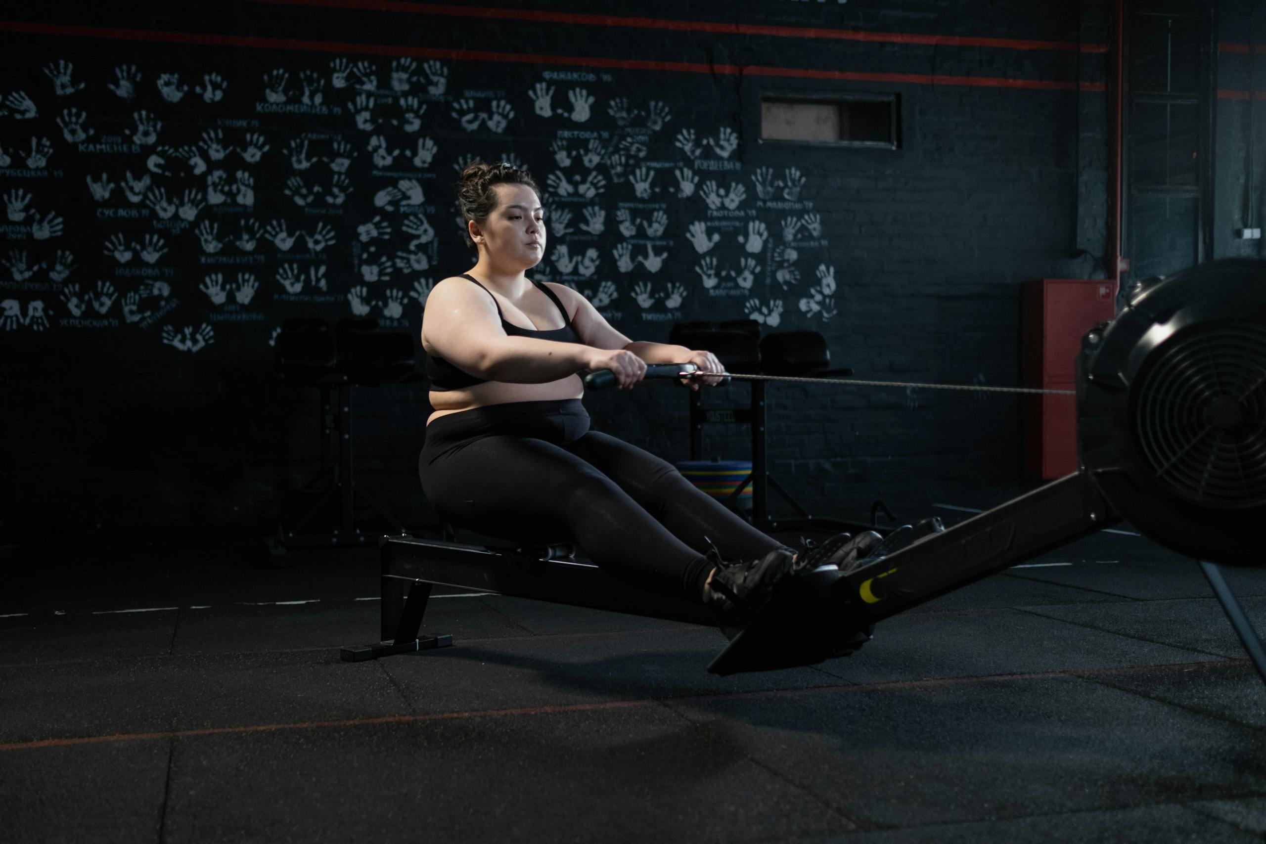 Plus-size woman working out on a rowing machine indoors, embracing fitness and a healthy lifestyle.