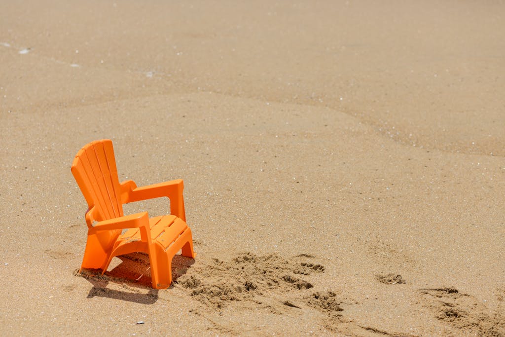 A vibrant orange plastic beach chair sits on a sandy shore under the sun, evoking a sense of tranquil seaside relaxation. Beach Chairs for Plus Size