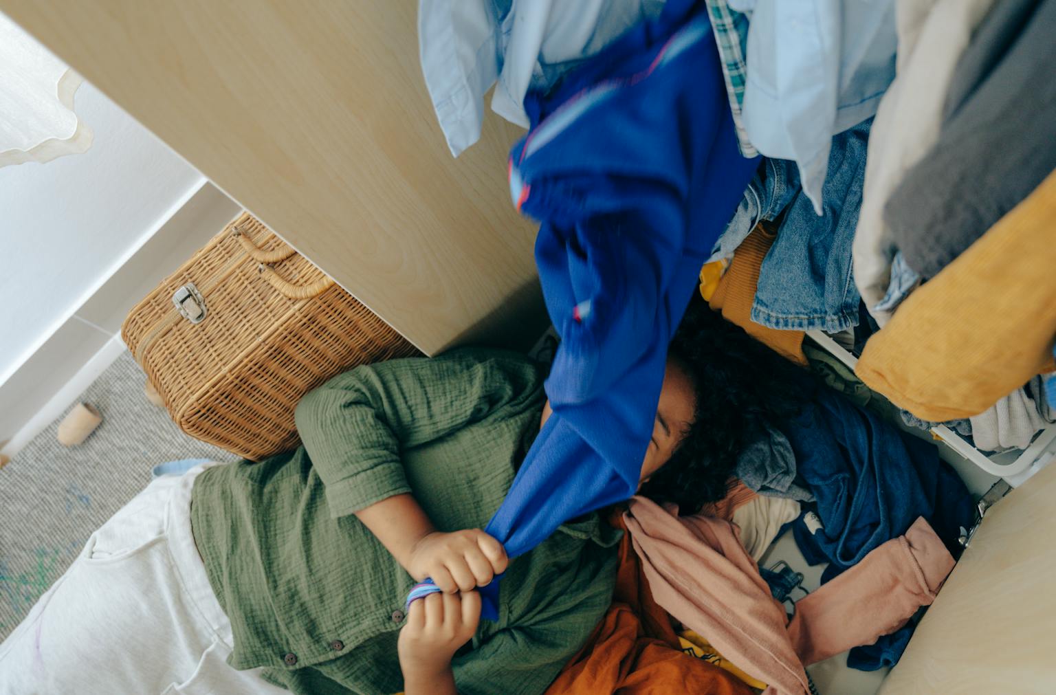 From above of faceless ethnic teenager having fun while arranging various clothes in wardrobe at home clean up your wardrobe