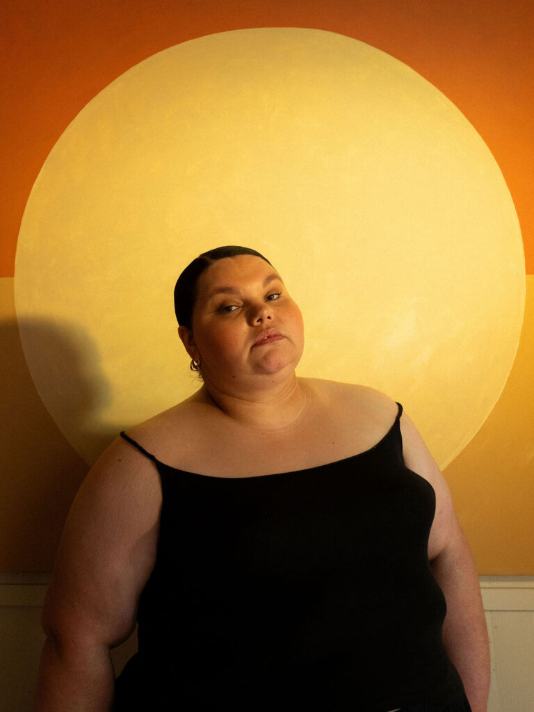 Kartanya Maynard posing in front of a glowing circular light during an editorial portrait session.

Kartanya Maynard plus size representation