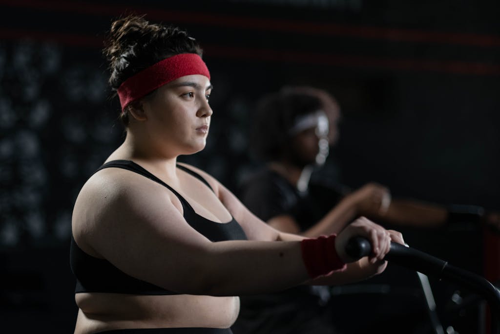 Determined woman in gym wear exercising on a stationary bike, exemplifying body positivity and fitness.

joyful movement
