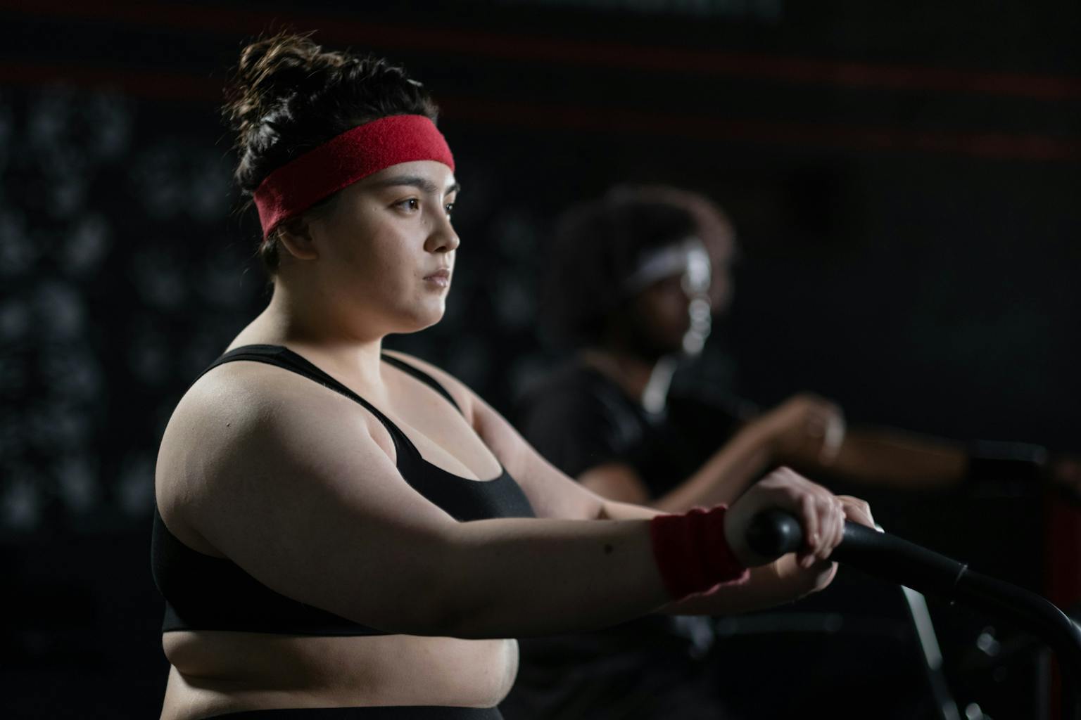 Determined woman in gym wear exercising on a stationary bike, exemplifying body positivity and fitness.

joyful movement