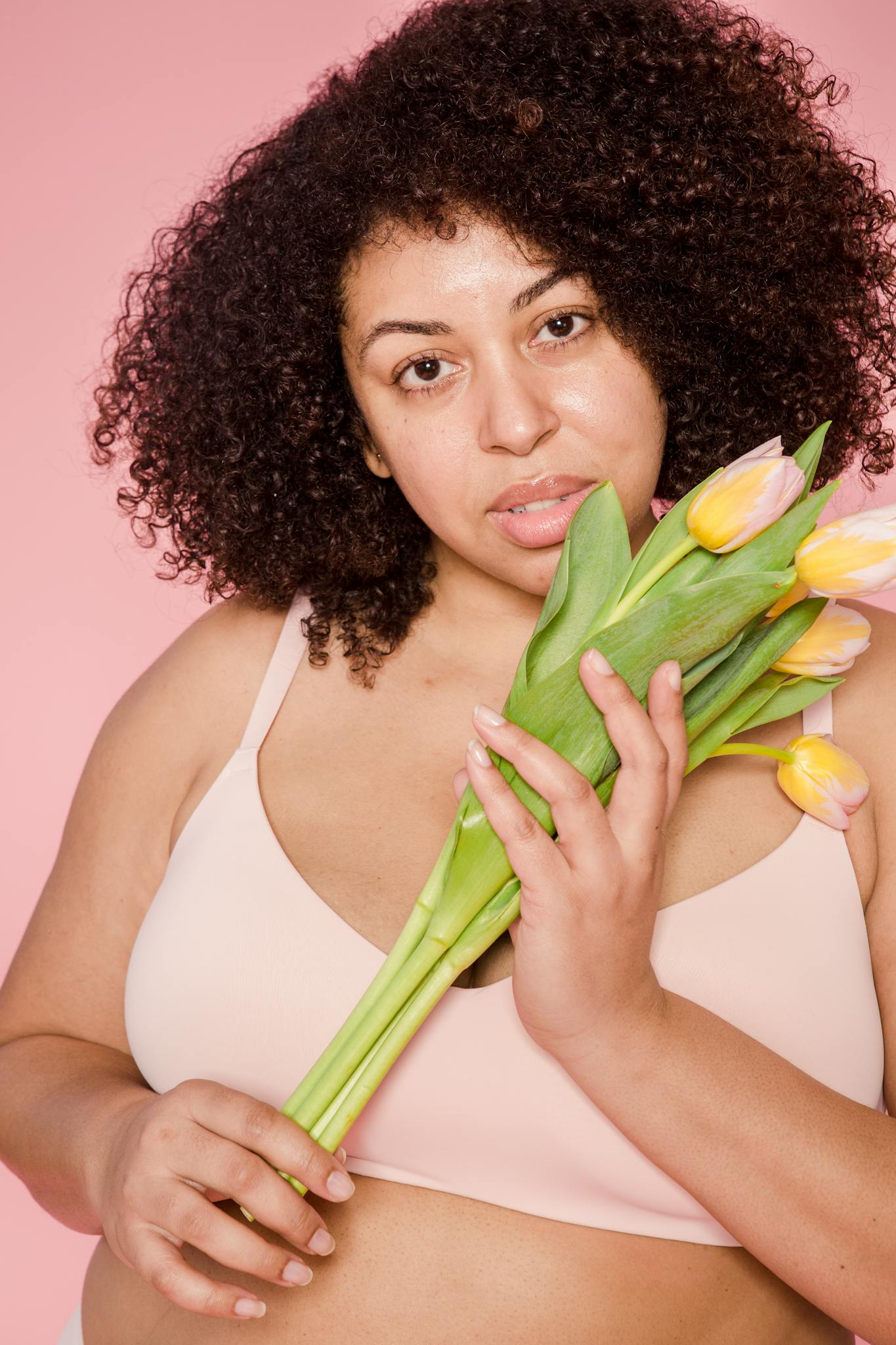 Plus size African American female model wearing beige lingerie looking at camera on pink background with fresh tulips in hands

Self-trust 