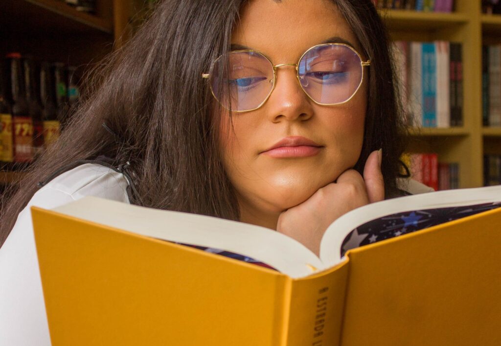 A focused woman enjoys reading a book in a cozy library setting, surrounded by bookshelves.