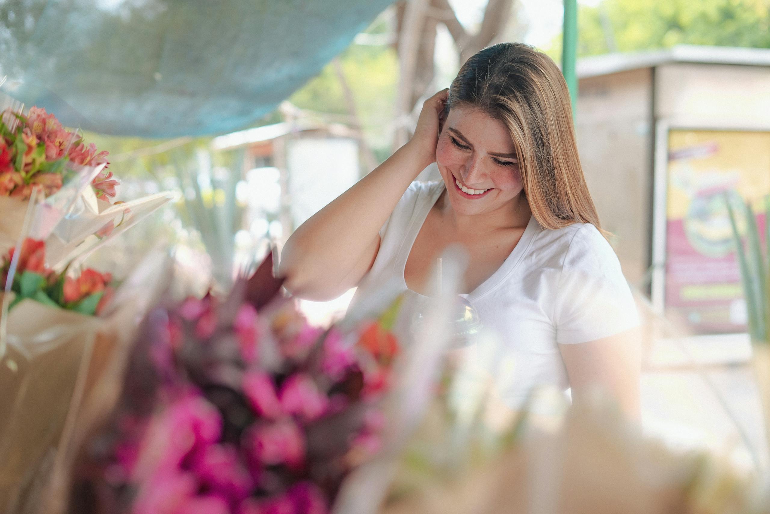 A happy woman in a white t-shirt enjoys browsing vibrant bouquets at a flower market.