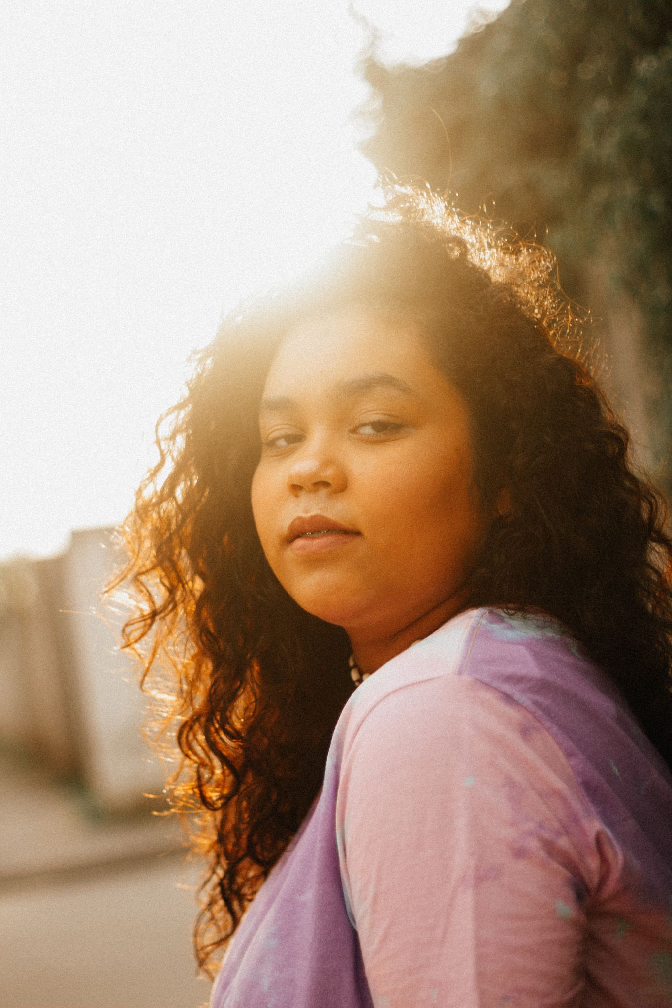 A serene outdoor portrait of a woman with backlit curly hair and a soft expression