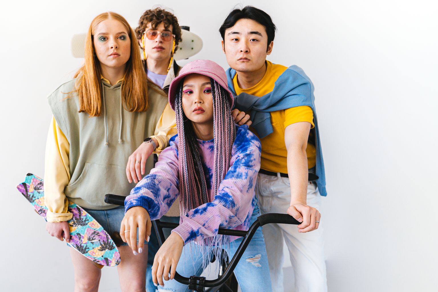 A trendy, diverse group of friends with unique fashion and hairstyles posing indoors with skateboards and a bike.