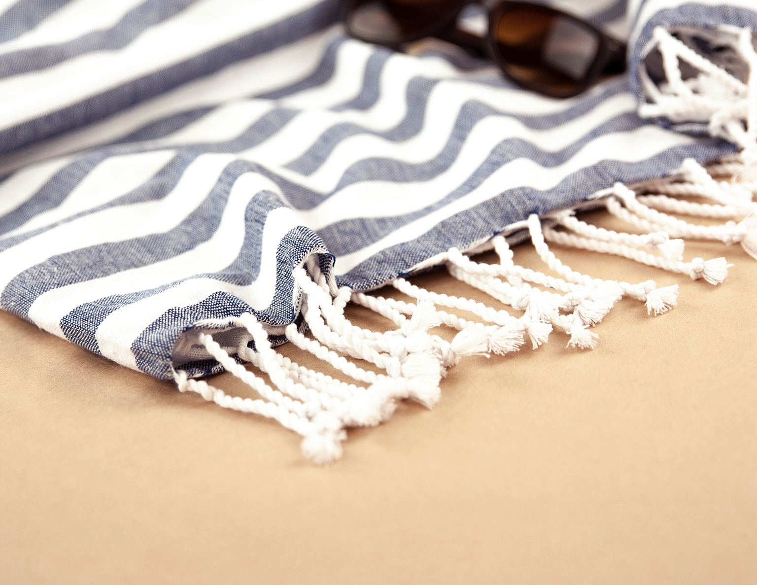 Close-up of a striped beach towel with sunglasses on sandy ground, ideal for a summer theme.