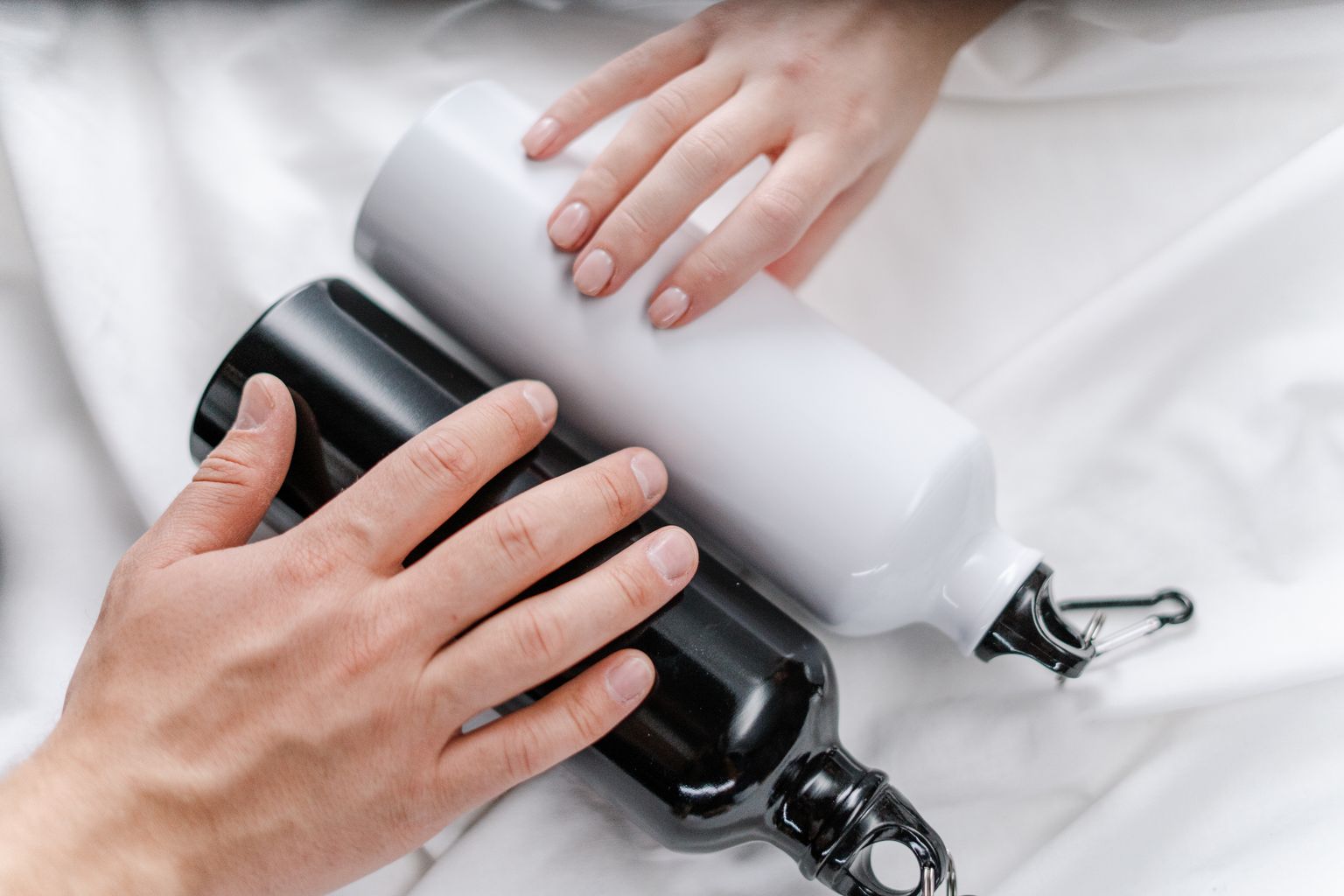 Close-up of hands holding reusable black and white tumblers on a white surface.