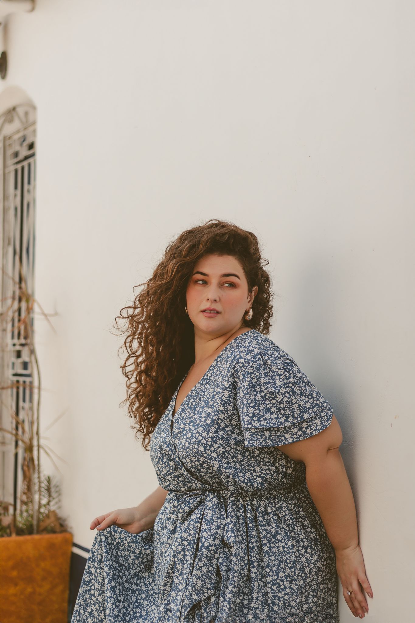 Confident woman with curly hair poses in a floral dress against a white wall in Rio de Janeiro.